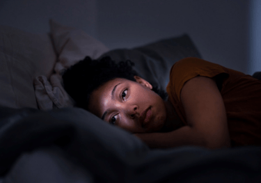 A young woman lying in bed at night suffering from insomnia and sleep deprivation.