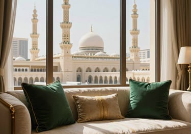 Professional architectural shot of a luxury hotel suite in Makkah. View through the window showing the minarets of the Grand Mosque. Interior features cream and gold linens with deep green cushions. Middle Eastern / Gulf style.