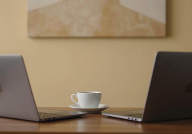 A professional desk setup in a warm South American / Brazilian / Bolivian office, featuring a laptop and a cup of coffee. The wall behind has a subtle warm sand colored art piece.