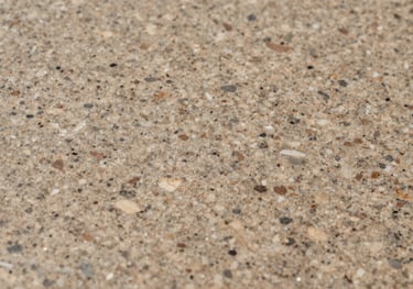A macro shot of a warm taupe granite surface with soft flecks of cream and muted brown, showing a honed finish that suggests professional reliability and natural beauty.