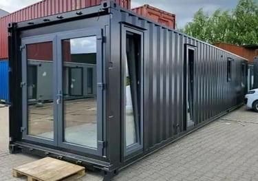 Modern black shipping container home with glass doors and windows on a paved lot.