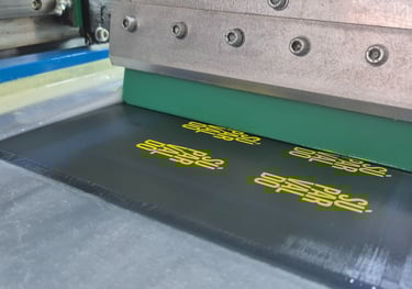 Automatic screen printing machine applying yellow ink onto a black textile panel with a green squeegee.