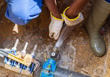 Plombier réparant à la clé un tuyau d'eau enterré dans une tranchée boueuse.