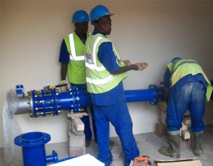 Trois ouvriers en gilets et casques posant un tuyau d'eau industriel bleu.