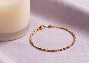 Detail shot of a minimalist candle and a delicate gold bracelet resting on a light lilac textured fabric. Elegant and warm lighting, South American aesthetic.