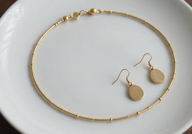 Top view of a gold necklace and a pair of minimalist earrings on a white ceramic plate. Feminine and refined South American style.