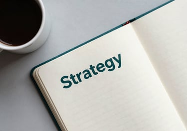 An overhead shot of a clean workspace featuring a cup of coffee and a notebook with 'Strategy' written on the first page, in muted teal and off-white.
