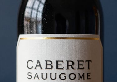 Close-up of a Cabernet Sauvignon bottle, focusing on the golden foil and the elegant typography of the label, set against a blurred dark blue background.