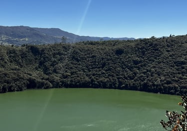 Panoramic view of Lake Guatavita, a green volcanic crater lake surrounded by lush forest in Colombia.