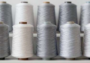 A series of Nylon yarn spools organized symmetrically on a shelf. The focus is on the smooth, lustrous surface of the thread. Colors featured include #95A5BB and soft grey.