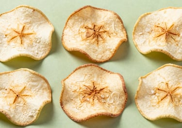 Macro photography of freeze-dried apple slices arranged neatly on a pale green background. The texture is sharp and detailed, showing the natural grain of the fruit.
