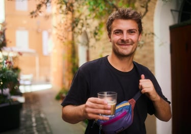 Aldan Kosnick holding a glass of coffe in a narrow alley