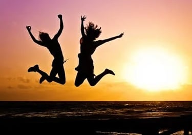 Two women's silhouettes jumping joyfully at sunset on the beach, full of energy