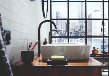 Modern bathroom vanity with a white vessel sink, matte black faucet, and a city view through a large window.