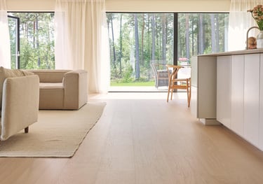 Modern open plan living room featuring light oak hardwood floors and large windows overlooking a forest.