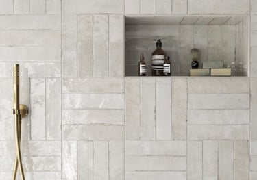 White gloss subway tile shower wall with gold hardware and built-in storage niche.