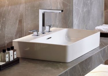 Modern white vessel sink with a chrome three-piece faucet on a grey marble bathroom vanity.