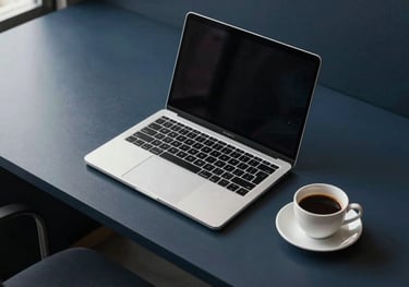 A clean, top-down shot of a minimalist workstation with a laptop and a coffee cup, set in a modern Southeast Asian / Indonesian office environment with dark navy blue accents.