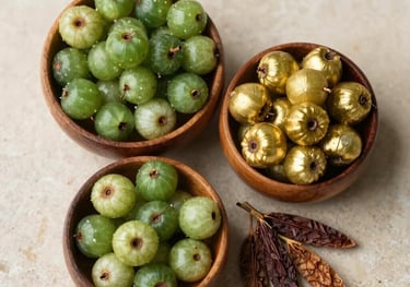 A top-down photo of three small wooden bowls filled with Amla, Haritaki, and Bibhitaki fruits, arranged on a cream-colored stone surface, South Asian / Indian herbalist style, deep green and warm gold accents.