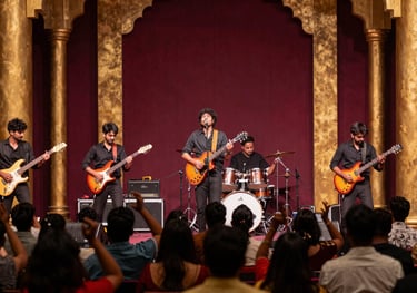 A high-energy live band performance on a modern stage with a South Asian / Indian audience dancing. Vibrant lights in antique gold and deep maroon.