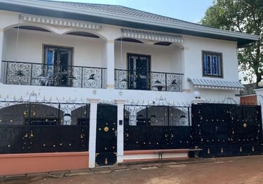 Maison blanche à étage, balcons en fer forgé noir et portail de sécurité assorti.
