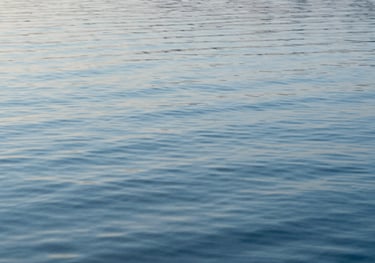 A serene photography of calm water ripples reflecting a light sky blue sky. The image is clean, abstract, and represents clarity and emotional well-being.