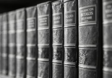 A high-contrast black and white close-up of a law library with leather-bound books. Professional and authoritative atmosphere. Uses #9CA4AA tones.