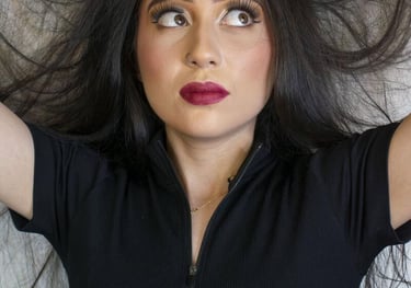 Una mujer con un atrevido lápiz labial rojo y cabello largo y oscuro posa mientras levanta su mechon