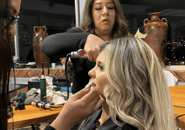 Maquilladora y peluquera profesional preparando a una mujer rubia para un evento especial.