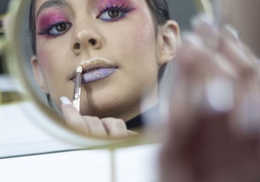 Una mujer aplica brillo labial con brillantina usando un pincel mientras se mira en un espejo 