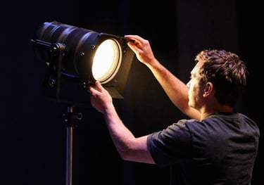 A professional stage technician adjusting a spotlight in a theater in the Pacific Northwest US. The scene uses dark navy shadows and warm gold highlights to convey professional integrity.