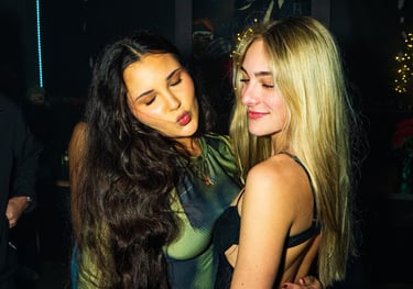 Two young women hugging and posing during a night out at a dimly lit bar or nightclub.