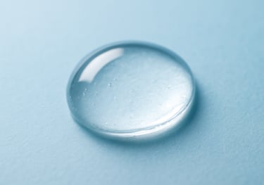 A macro photograph of a drop of clear, viscous essence reflecting light, showing the pure and concentrated nature of Korean skincare technology. Clean and clinical aesthetic with a light blue tint.