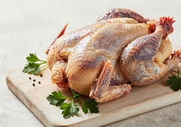 A rustic but clean arrangement of fresh farm poultry and herbs on a light cream wooden board. Sophisticated lighting emphasizing texture and freshness.