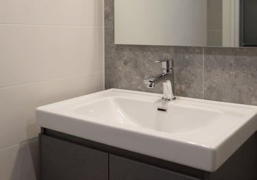 A clean, modern bathroom in a furnished apartment, showcasing high-quality fixtures and a minimalist design in soft off-white and dark slate grey tones.