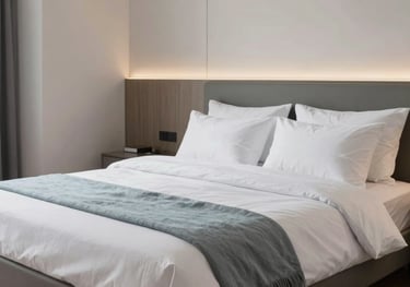 A modern bedroom in a furnished apartment, featuring a comfortable bed with clean white linens and light blue-grey accents, Zentraleuropäisch / Deutsch style.