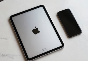Top-down view of a modern silver tablet and smartphone on an off-white marble desk, clean and tech-focused aesthetic.