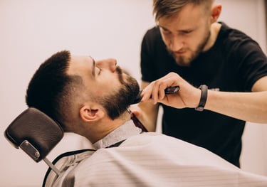 Professional barber grooming a client's beard with a comb at a modern barbershop.