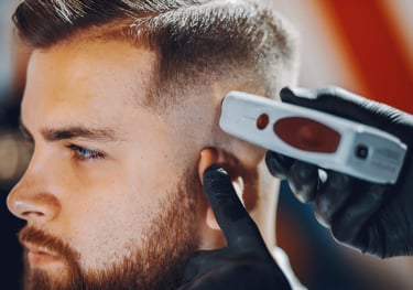 Professional barber using electric hair clippers to give a man a precise skin fade haircut.