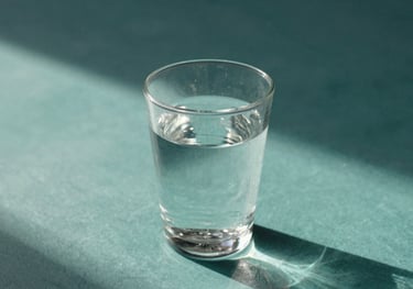 A high-quality still life photography representing mental clarity, featuring a clear glass of water on a teal surface with soft shadows and morning light, Latin American setting.