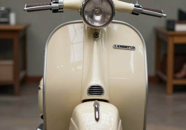 A front-angle studio photograph of a restored Lambretta LD from the 1950s. The scooter is painted in a soft cream color with chocolate brown leather seats. The lighting is clean and professional, emphasizing the iconic round headlight and the sleek front mudguard. Authentic Brazilian workshop setting in the background.