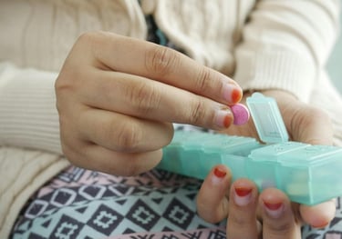 A person taking a pink pill from a green daily medication organizer for health management.