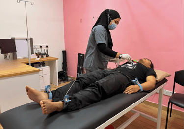 A nurse performing an ECG heart test on a patient in a medical clinic with pink walls.