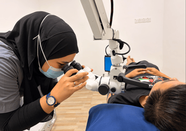 A female dentist in a hijab using a dental microscope to examine a patient during a procedure.