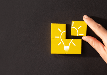 a person's hand holding a yellow light bulb on a black table