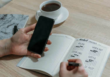 a person holding a cell phone and writing on a notebook