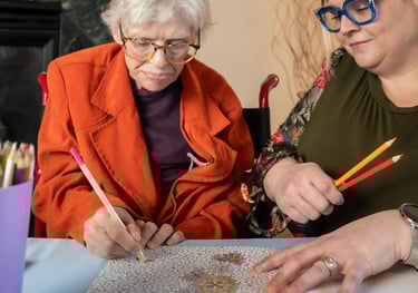 A senior woman and a caregiver participating in art therapy by coloring in a floral adult coloring book.