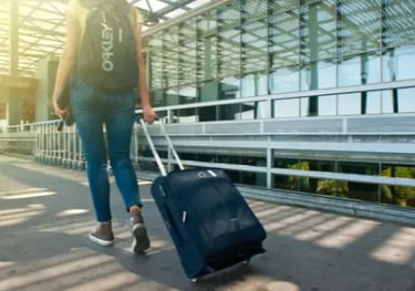 A woman pulling a blue rolling suitcase at a modern airport terminal for travel.