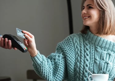 Smiling woman using a credit card for a contactless payment on a mobile card reader in a cafe.