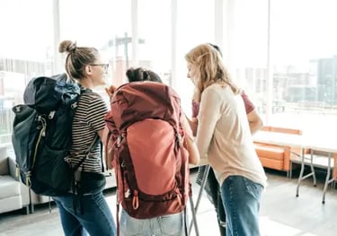 A group of young backpackers talking in a modern hostel lounge while planning their travel route.